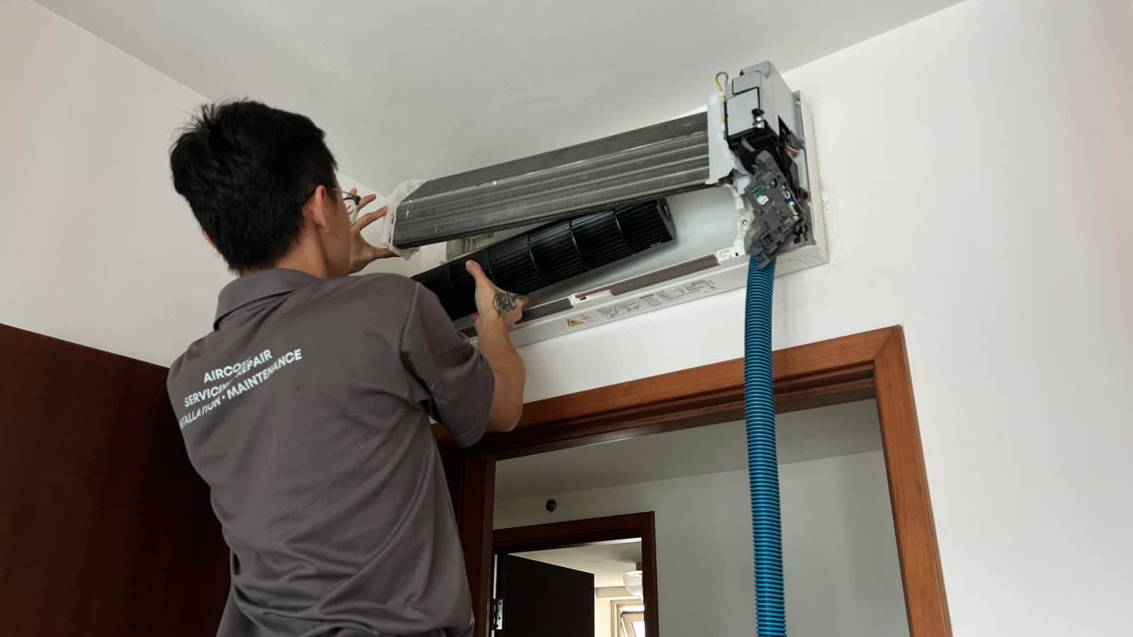 Technician vacuuming an aircon drainage line clear, the suction hose running to the indoor unit